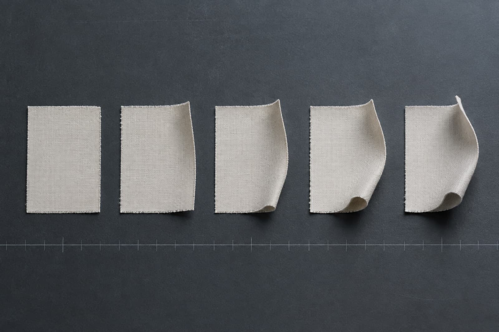 Five identical fabric swatches in a row on a dark measured plate, each lifted a little further at one edge than the last.